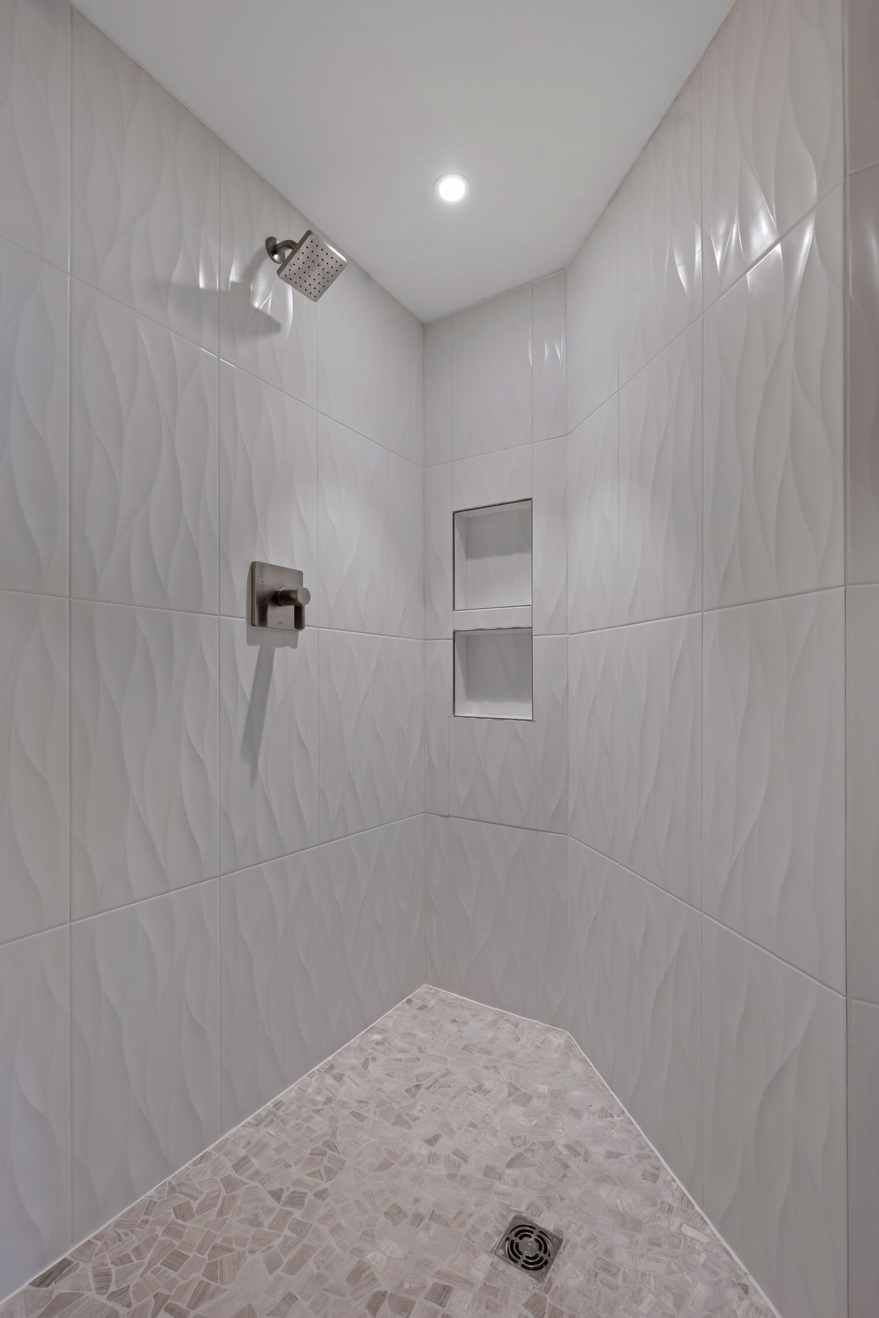 Walk-in shower detail with sculpted wave tile, recessed niches, and pebble-stone floor