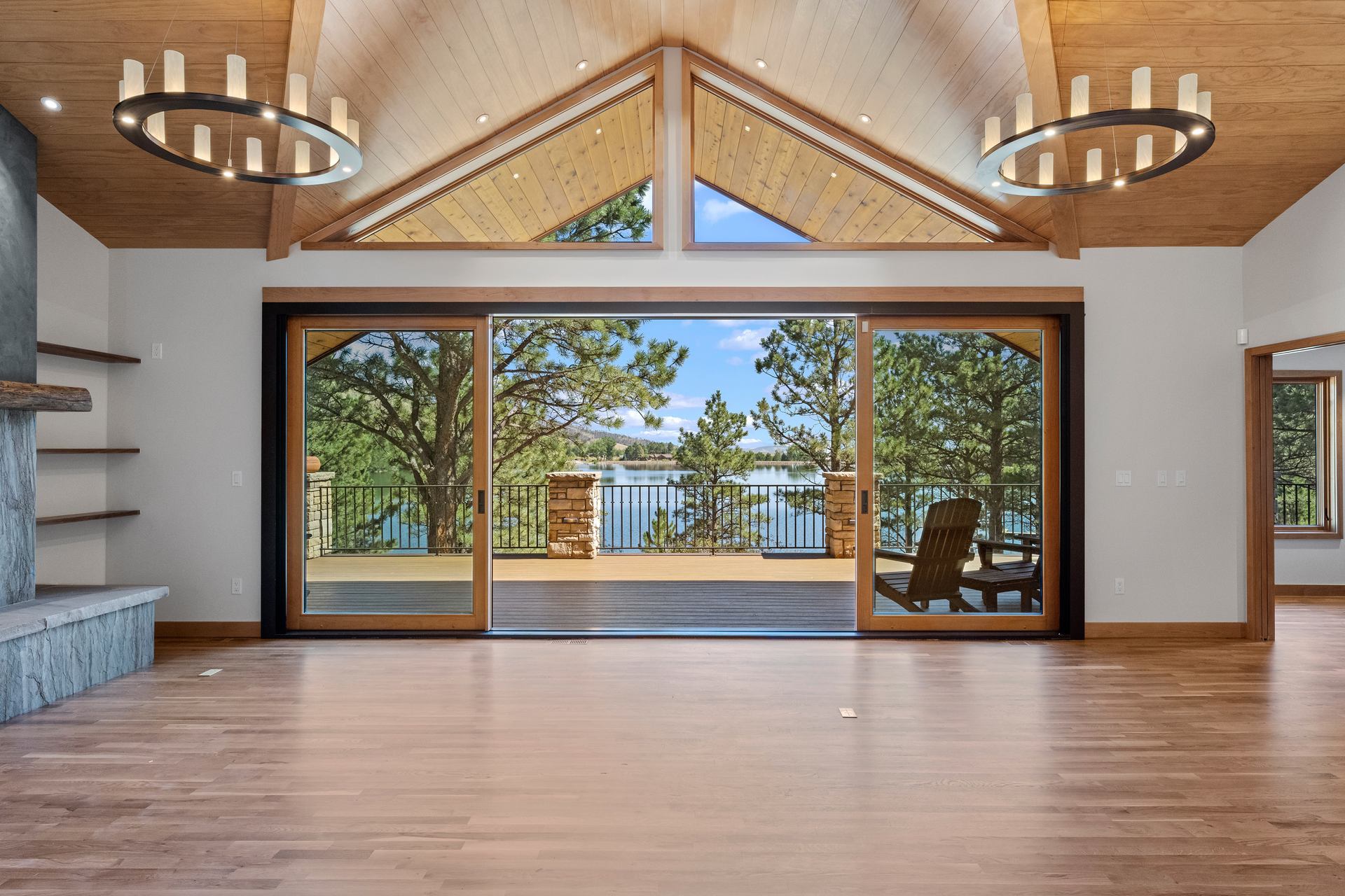 Vaulted great room with wood-clad ceiling and sliding glass walls opening to a lakeview deck