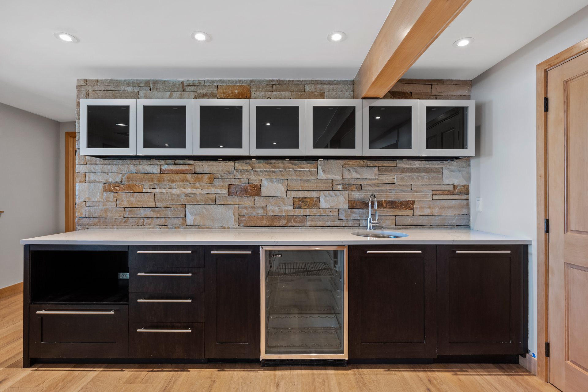 Finished lower level with stacked-stone bar wall, beverage center, and glass-front cabinets
